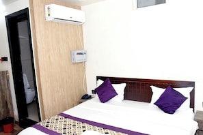 A hotel room with a bed, a wooden headboard, a wall-mounted air conditioner, a bedside phone, and a visible door leading to a bathroom. - RR PALACE (Gorakhpur)