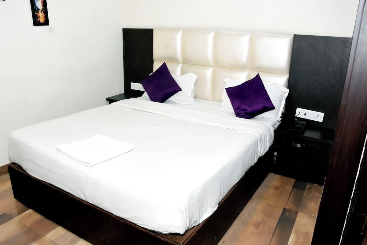 Una cama bien tendida con sábanas blancas, un cabecero acolchado y dos almohadas moradas.