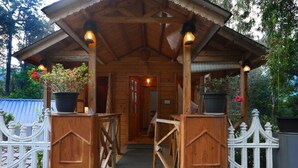A wooden gazebo with a roof, potted plants, and a white picket fence.