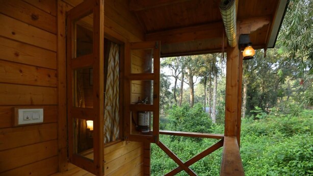 A wooden cabin with a large open window, a wooden door, and a small shelf with a container.
