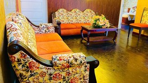 A room with floral-patterned sofas, a wooden wall, and a small table with flowers.