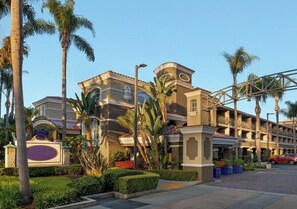 A hotel with a Mediterranean architectural style, featuring a central courtyard with palm trees and a red car parked outside. - Poolside Anaheim Retreat Near Disneyland & Honda Center (Anaheim)