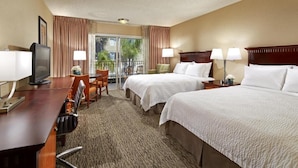 Ein Hotelzimmer mit zwei Betten, einem Schreibtisch mit Computer, einem Stuhl und Blick ins Freie.