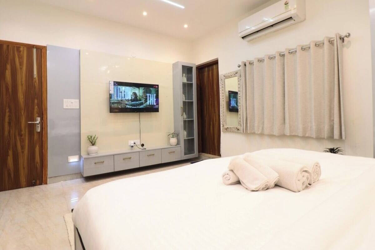 A modern bedroom with a large bed, a TV mounted on the wall, a wardrobe, and a mirror.