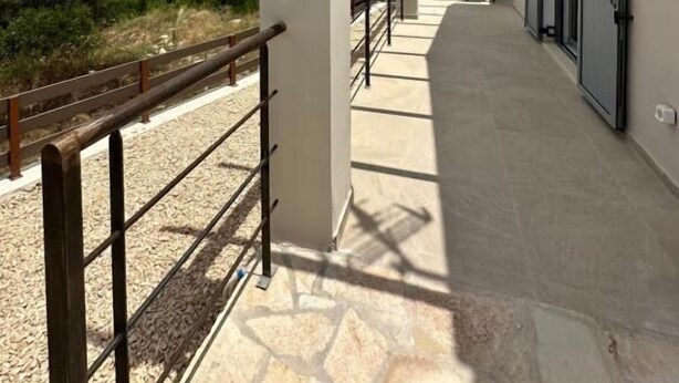 A covered outdoor corridor with a stone floor, white pillars, and a wooden railing. - Scandal House by All About Paxos (Paxos)