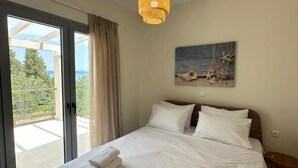 A bedroom with a bed, a painting, a hanging light fixture, and a view through a glass door. - Scandal House by All About Paxos (Paxos)