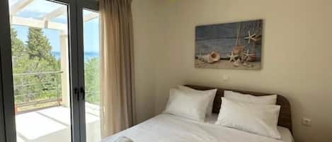 A bedroom with a bed, a painting, a hanging light fixture, and a view through a glass door.