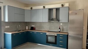 A modern kitchen with grey cabinets, a stainless steel refrigerator, and a built-in oven. - Scandal House by All About Paxos (Paxos)