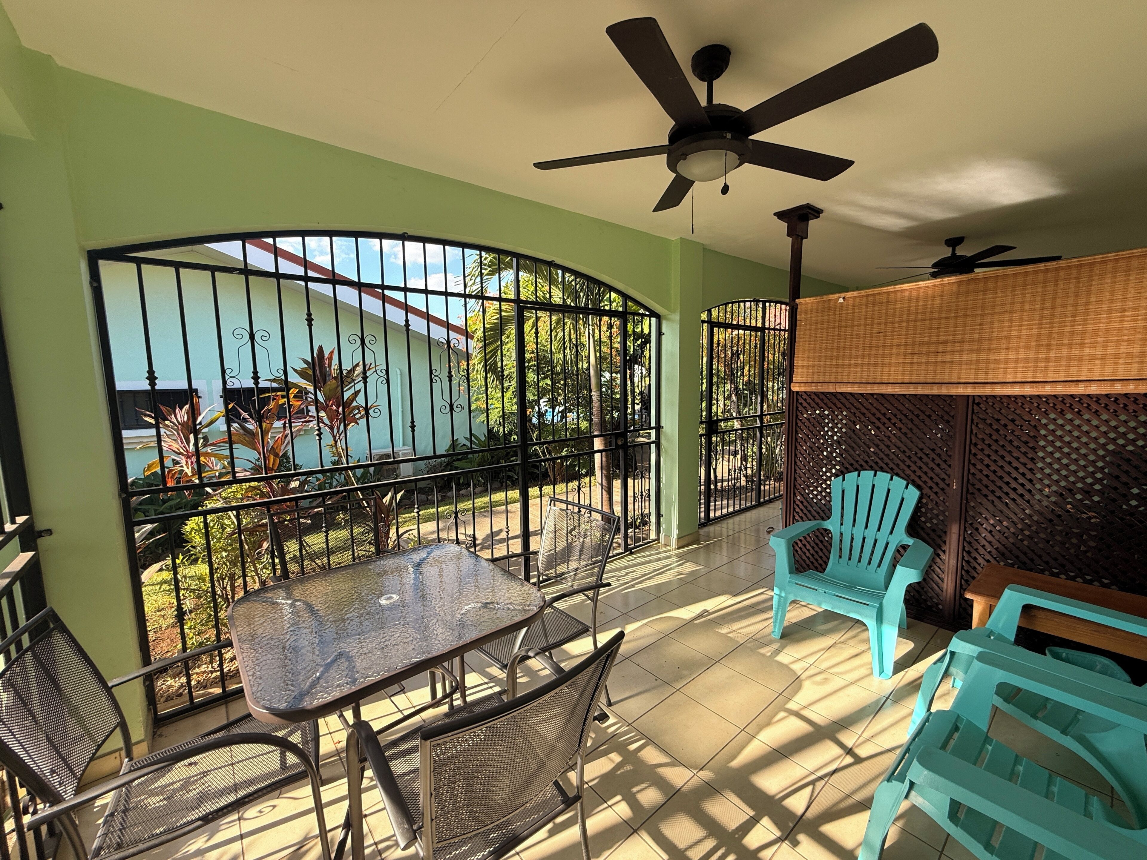 A balcony with a table and chairs, a ceiling fan, and a view of greenery and a building.