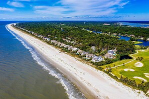 Ett flygbildsbild av ett bostadsområde vid kusten med fastigheter som ligger direkt vid stranden, en golfbana och en sjö.