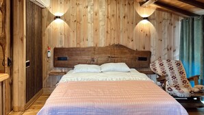 A wooden cabin room with a bed, two wall-mounted lights, a chair, and a window with curtains.