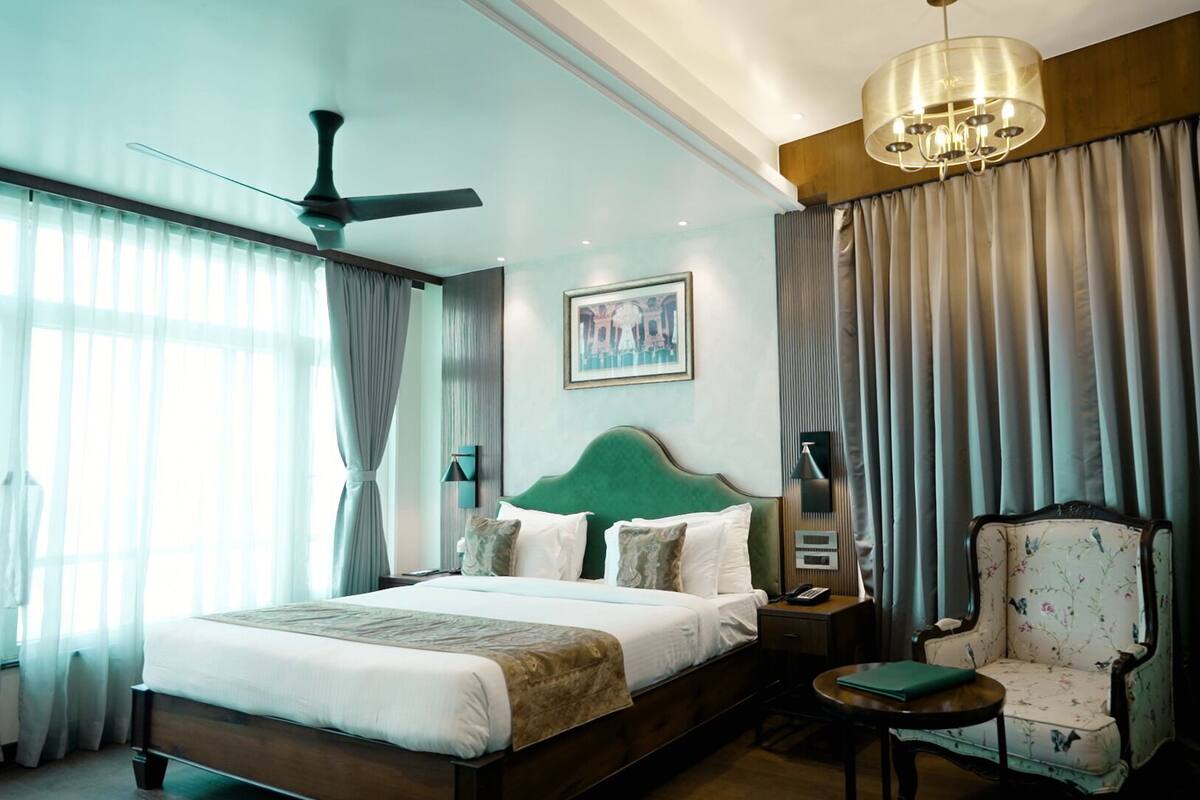 Habitación de hotel con cama, una silla, un escritorio, un ventilador de techo, una araña y cortinas.