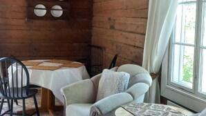 Une pièce chaleureuse avec des murs en bois, une table à manger, deux fauteuils, une petite table ronde et une fenêtre avec des rideaux.
