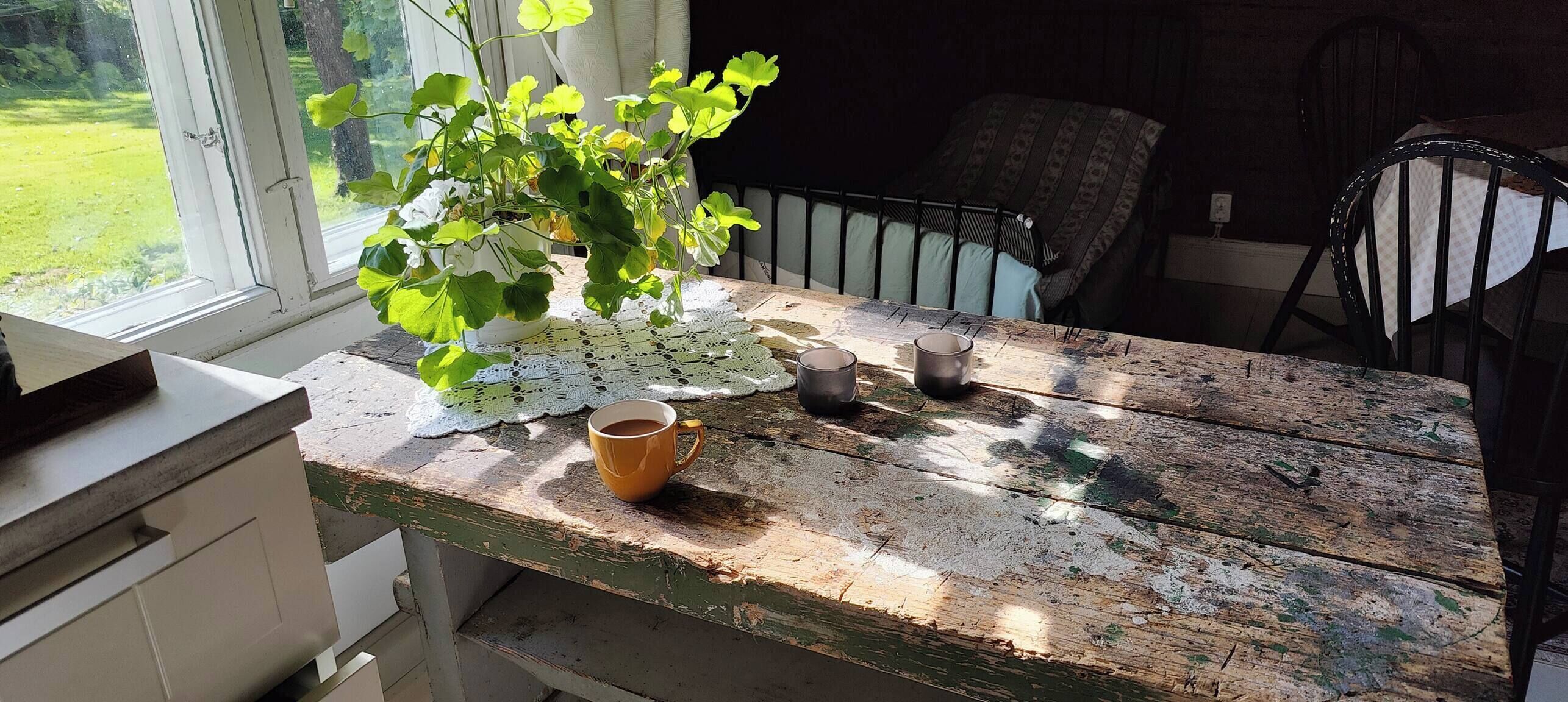 Une table en bois rustique, ornée d’un chemin de table en dentelle, d’une plante en pot et de deux tasses.