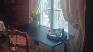 Un intérieur en bois avec une table, des chaises, une fenêtre avec des rideaux et une plante en pot aux fleurs jaunes.