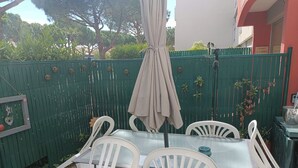A patio with a table and chairs, a green fence, and a building in the background. - T2 cabin with terrace, close to beach and port, all amenities on foot (Saint-Cyprien)