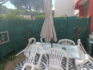 Eine Terrasse mit Tisch und Stühlen, ein grüner Zaun und ein Gebäude im Hintergrund.