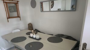 A dining table with a modern design, a small decorative shelf, and a mirror on the wall. - T2 cabin with terrace, close to beach and port, all amenities on foot (Saint-Cyprien)