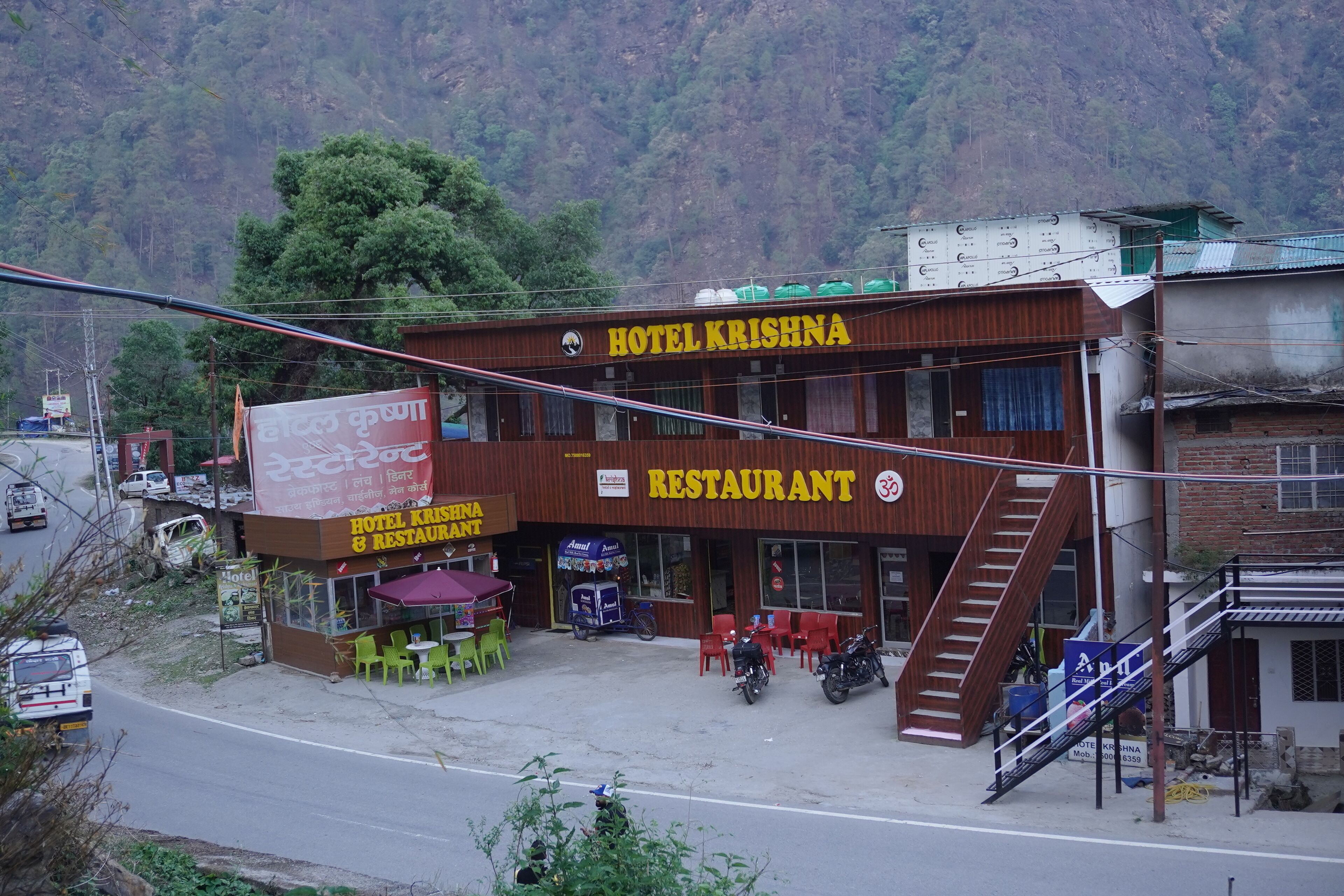 A two-story building with a sign for 'Hotel Krishna & Restaurant' and a staircase leading to the upper floor.