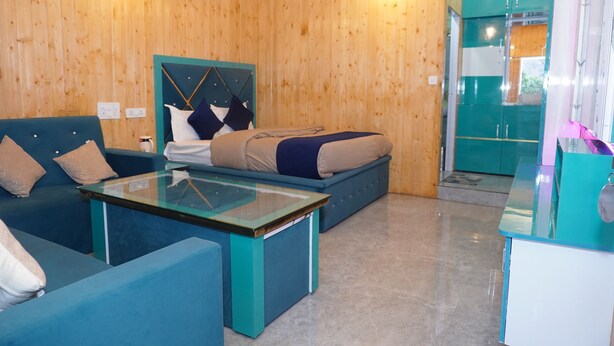 Una habitación con una cama, dos sofás, una mesa de vidrio, paredes de madera y una kitchenette.