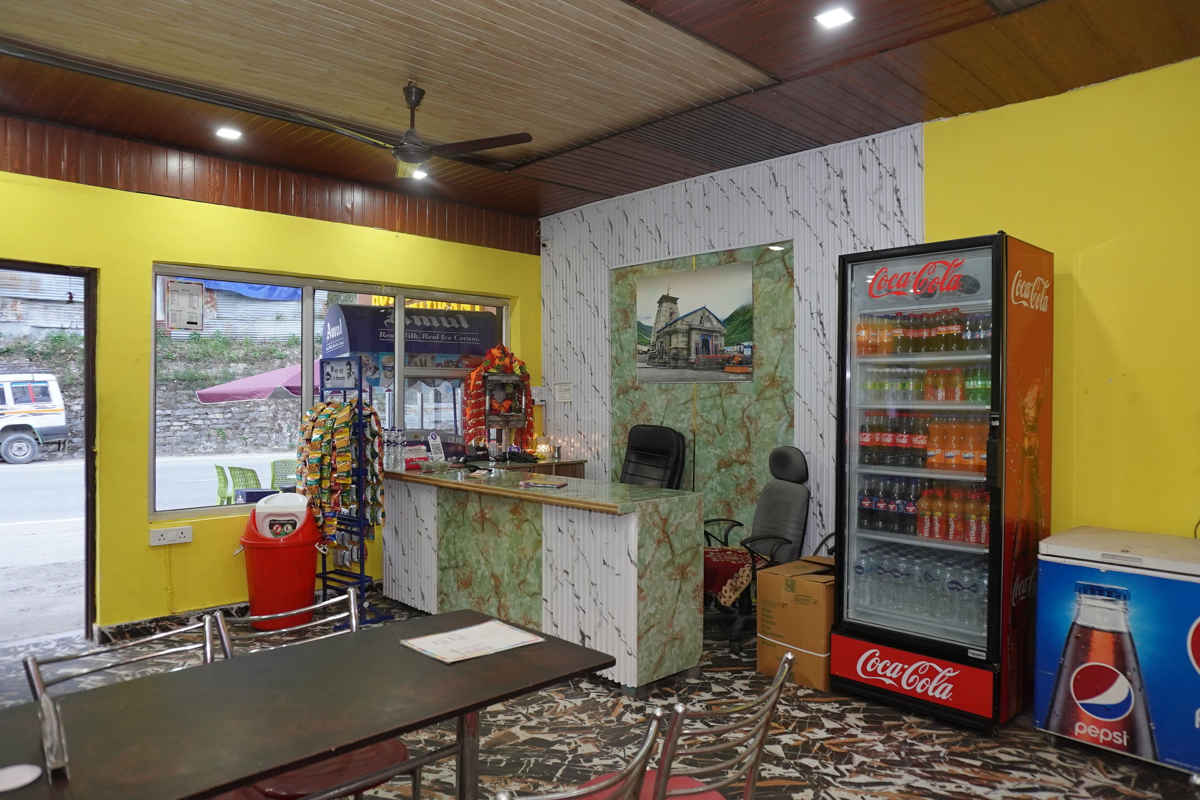 A restaurant interior with a Coca-Cola refrigerator, a counter with a decorative item, and a view through the window.