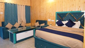 Una habitación con paredes de madera, una cama con cabecera, dos sofás azules, una mesa de vidrio y cortinas.