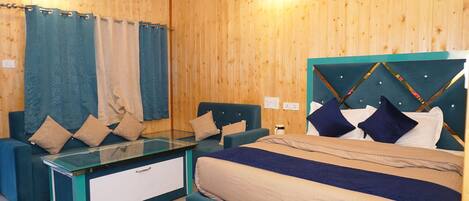A room with wooden walls, a bed with a headboard, two blue sofas, a glass table, and curtains.