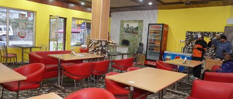 A restaurant with red chairs and tables, a Coca-Cola refrigerator, and a wooden pillar.