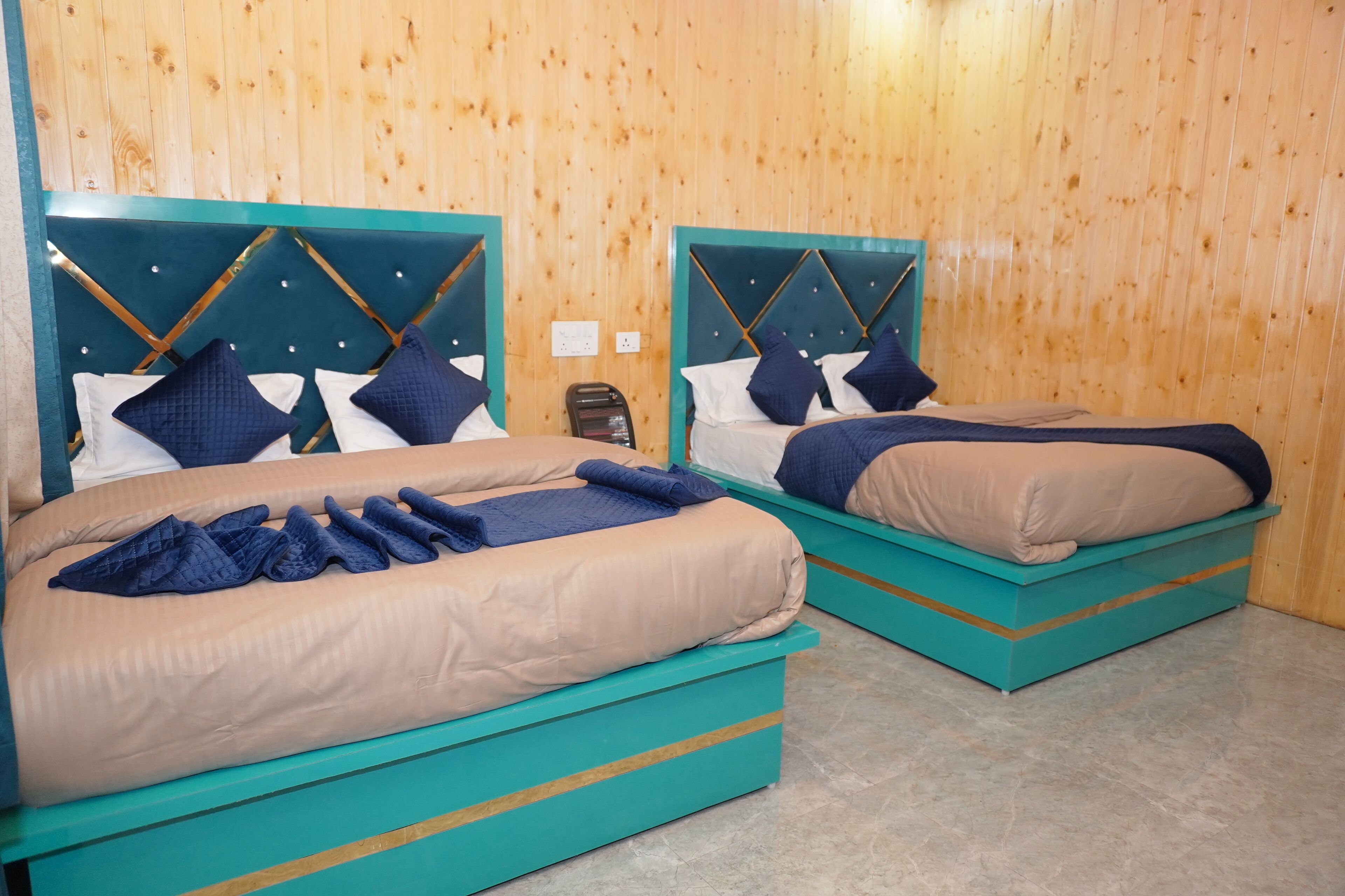 Two beds with teal headboards and blue bedding in a room with wooden walls.