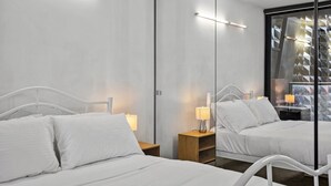 A hotel room with two beds, bedside lamps, a mirror, and a view of a building with geometric patterns. - Central 2 Bed Apartment Near Melbourne CBD (Melbourne)