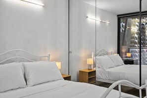 A hotel room with two beds, bedside lamps, a mirror, and a view of a building with geometric patterns. - Central 2 Bed Apartment Near Melbourne CBD (Melbourne)
