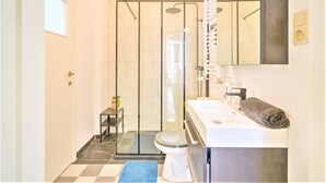Une salle de bain avec une douche à parois de verre, un lavabo blanc et une serviette posée sur le comptoir.