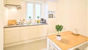 Une cuisine avec des armoires blanches, un plan de travail en bois, une fenêtre, un four à micro-ondes, une machine à café et une table avec des chaises.