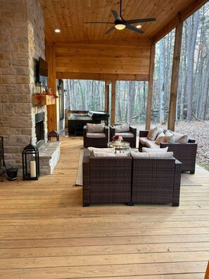 A covered outdoor seating area with wicker furniture, a fireplace, and a view of the forest. - Welcome to our cozy cabin-Mountain Delight on the Georgia/Tennesse border. (McCaysville)