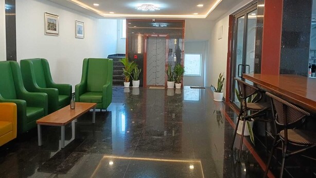 Eine Lobby mit grünen Stühlen, einem Holztisch, einem Empfangsbereich und einer Treppe, die zu einem Aufzug führt.