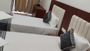 Ein Hotelzimmer mit zwei Betten, einem Nachttisch, einem Fenster mit Vorhängen und einer Wand-Klimaanlage.
