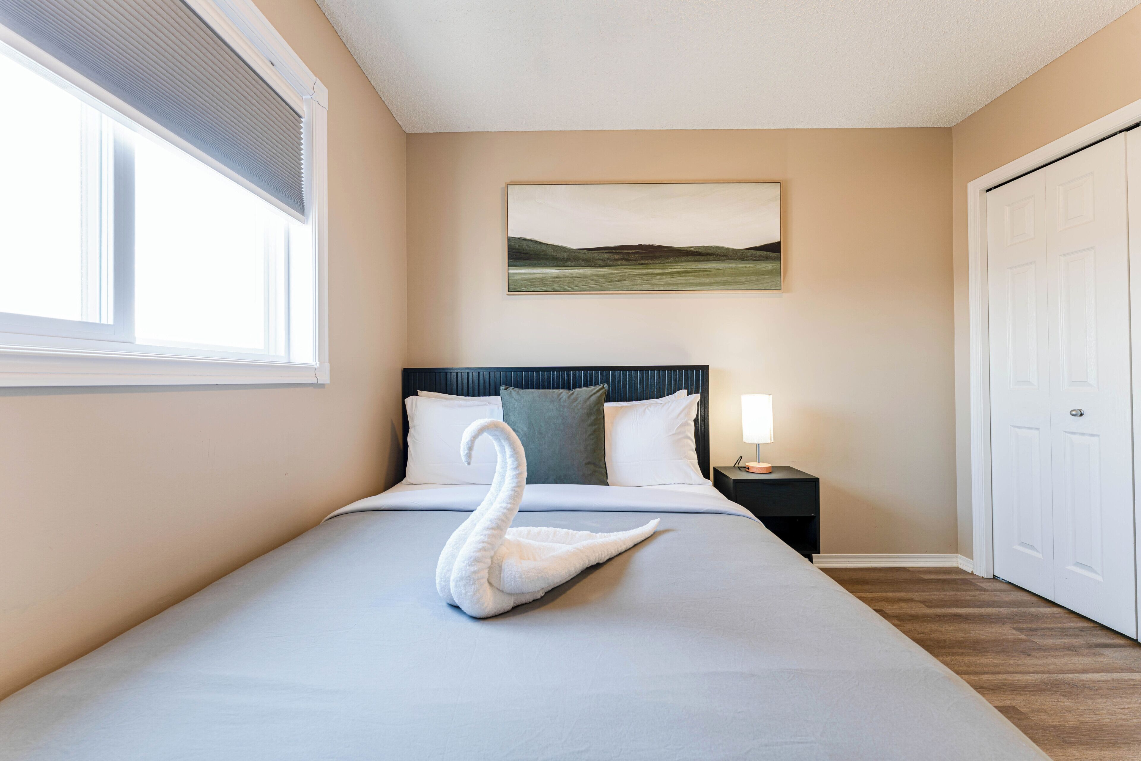A hotel room with a bed, a nightstand, a lamp, a painting on the wall, and a door.