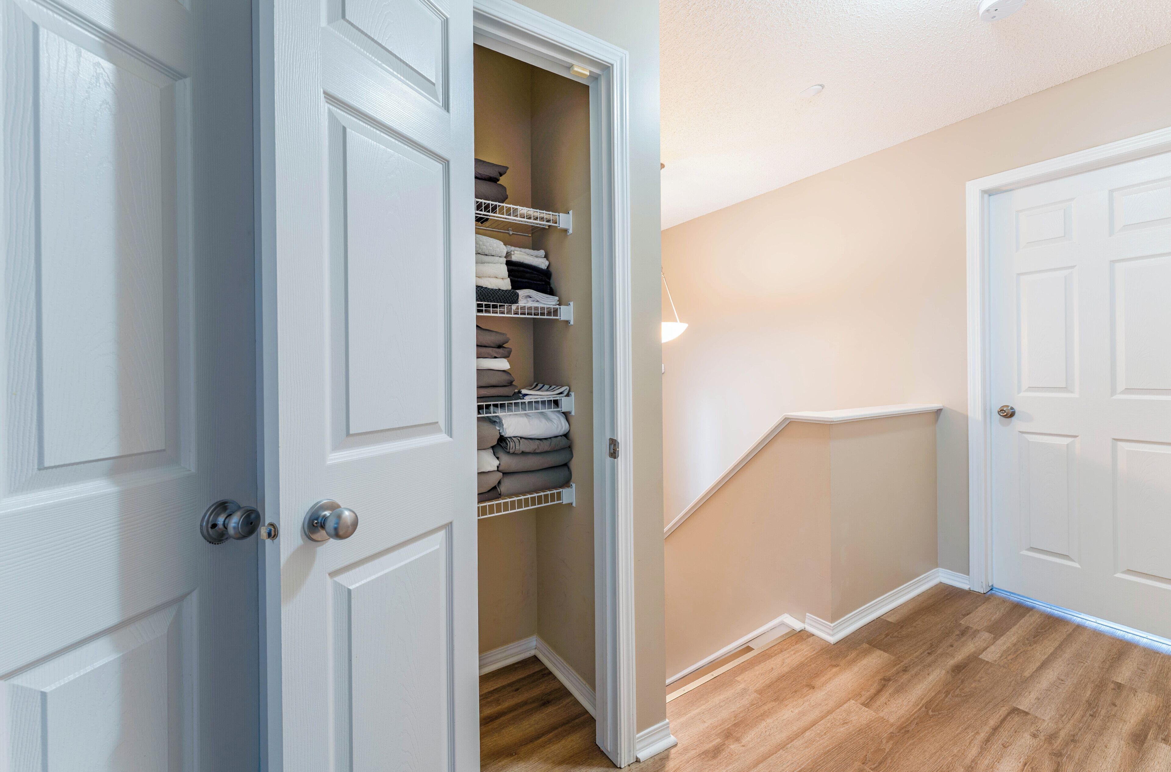 A hallway with a white door, a wooden floor, and a closet with shelves.