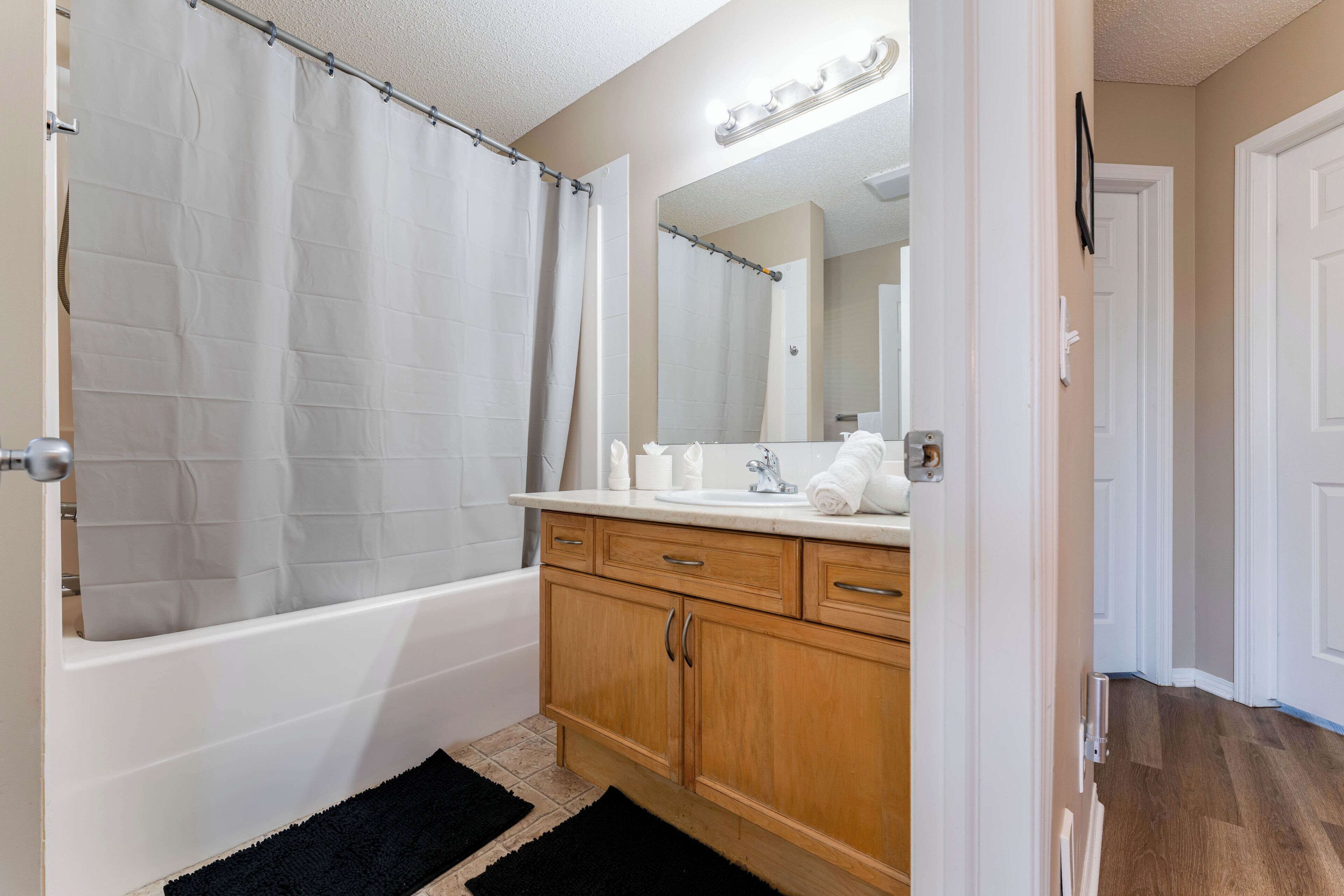 A bathroom with a bathtub, a sink, a mirror, and wooden cabinets.