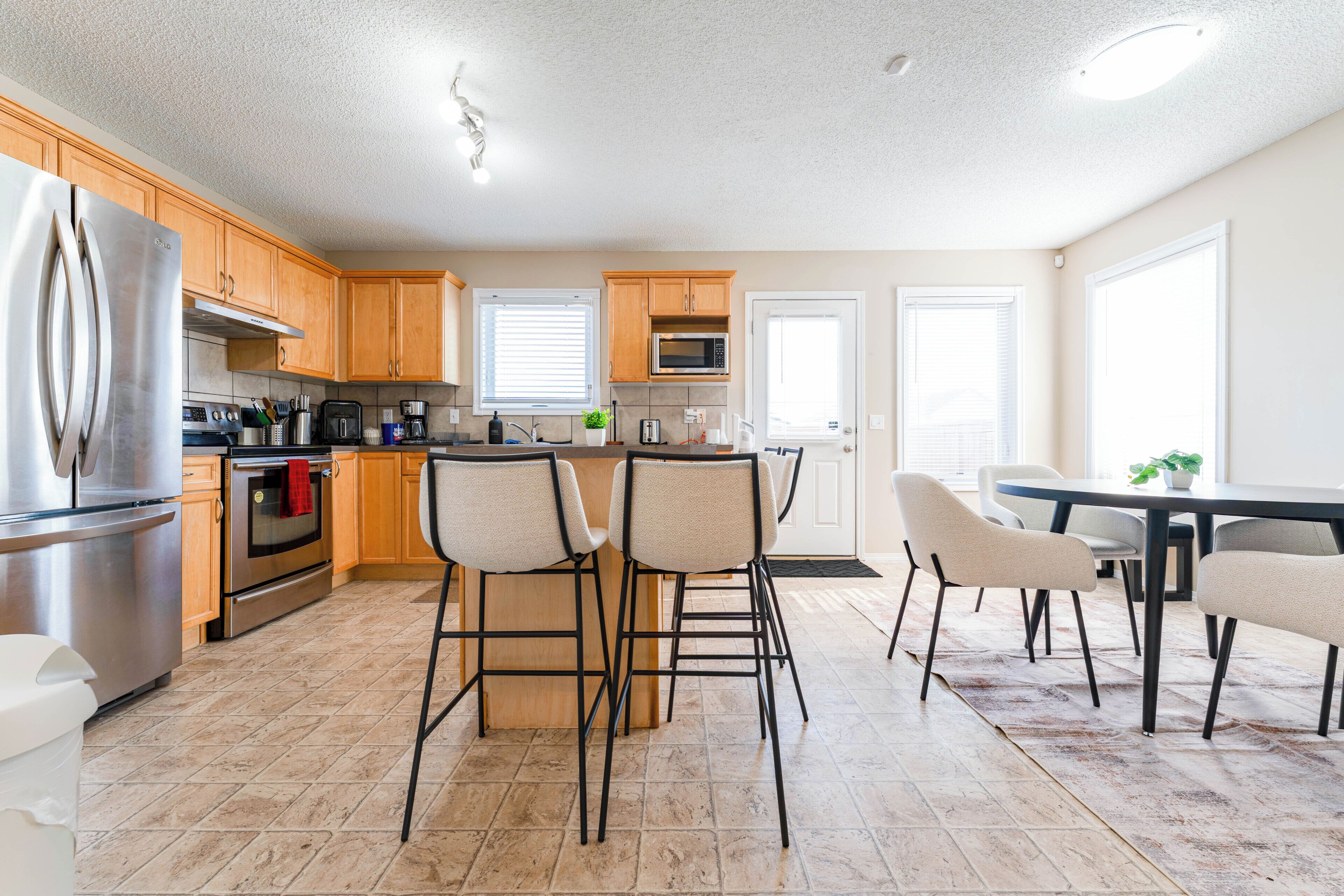 A modern kitchen with stainless steel appliances, wooden cabinets, and a dining area with bar stools.