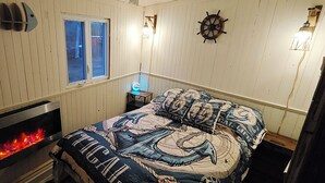 Ett rum med en säng, en öppen spis, ett fönster och väggdekorationer med marint tema.