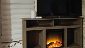 Ett vardagsrum med en öppen spis, en tv-apparat på ett träbord och en vit dörr.