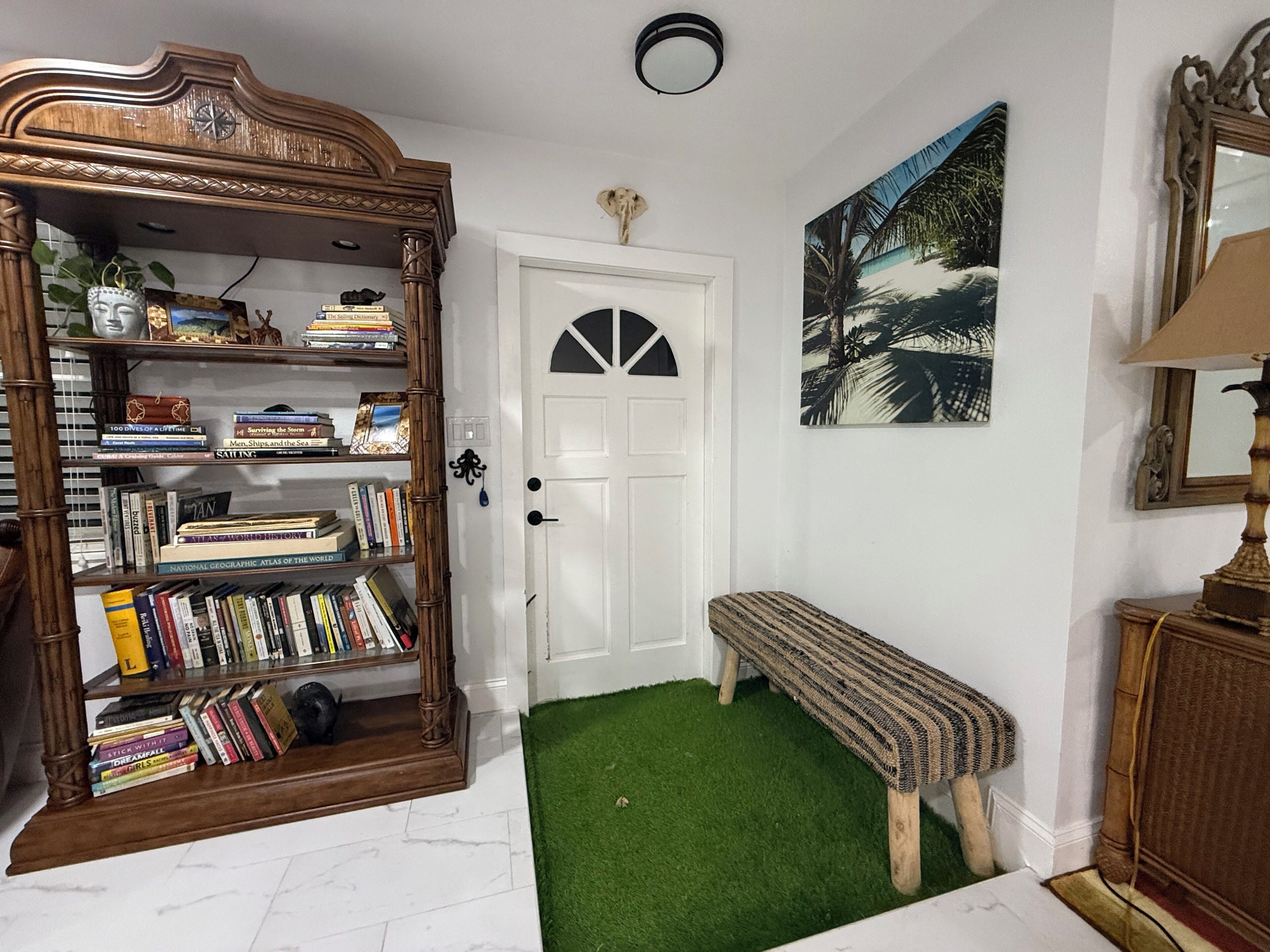Una habitación con una estantería de madera, una puerta blanca, un banco, un cuadro y una lámpara.