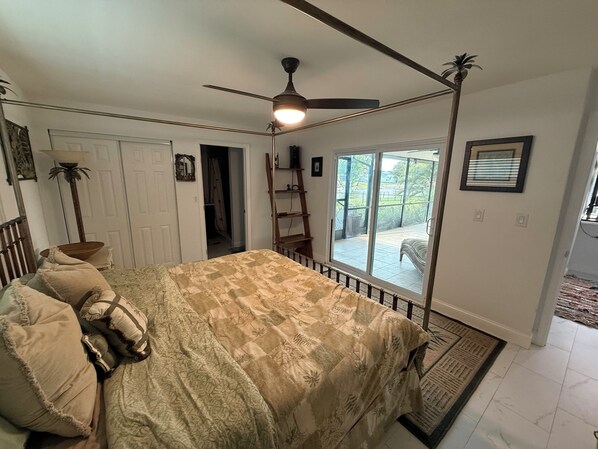 A bedroom with a bed, a ceiling fan, a large window, and a door leading to a balcony. - Fort Myers waterfront home (Fort Myers)