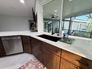 A modern kitchen with a dishwasher, wooden cabinets, a large window, and a ceiling fan.
