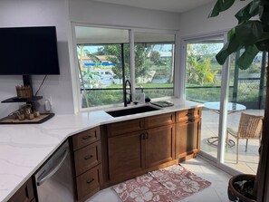 A modern kitchen with a large window, wooden cabinets, and a built-in dishwasher.
