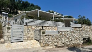 A stone-walled building with a gated entrance, a covered outdoor area, and a clear sky. - Rouli's Houses by All About Paxos (Paxos)