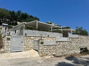 A stone-walled building with a gated entrance, a covered outdoor area, and a clear sky. - Rouli's Houses by All About Paxos (Paxos)