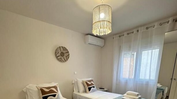 A hotel room with two single beds, a small table, a chandelier, an air conditioning unit, and a view of the outside. - Rouli's Houses by All About Paxos (Paxos)