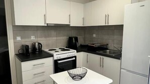 A compact kitchen with white cabinets, a stove, a coffee maker, and a small table with chairs. - Rouli's Houses by All About Paxos (Paxos)
